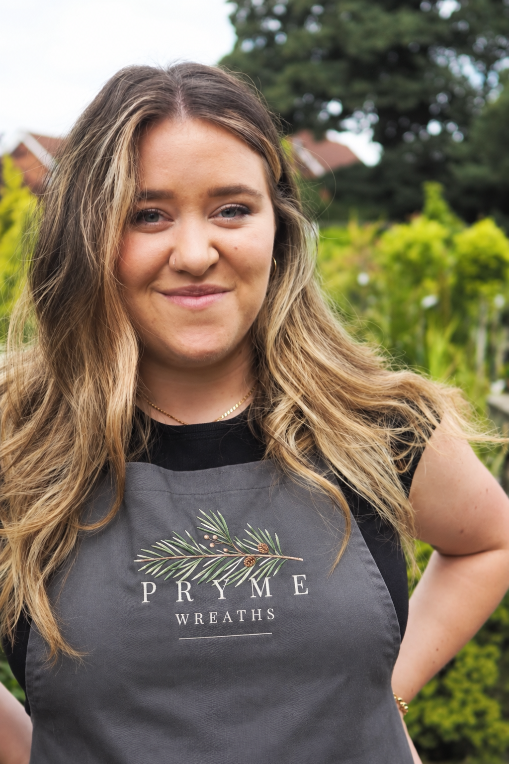 Isla, the maker behind Pryme Wreaths, wearing her branded apron in a garden